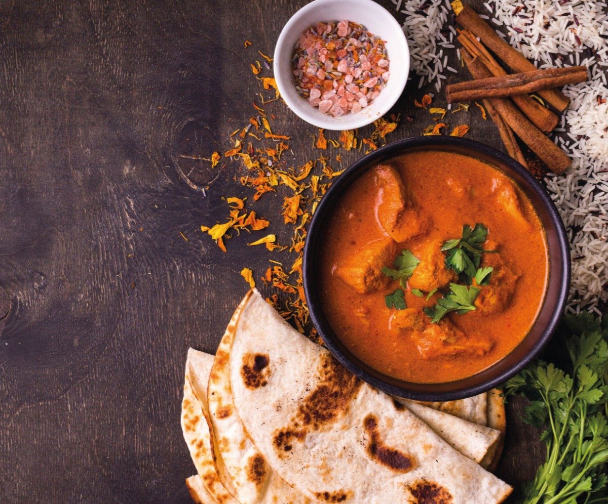Traditional Indian Curry from Taste of India, Sheerness Bowl of Chicken curry with naan on the side, table garnished with cinnamon sticks, pink rock salt, coriander and rice